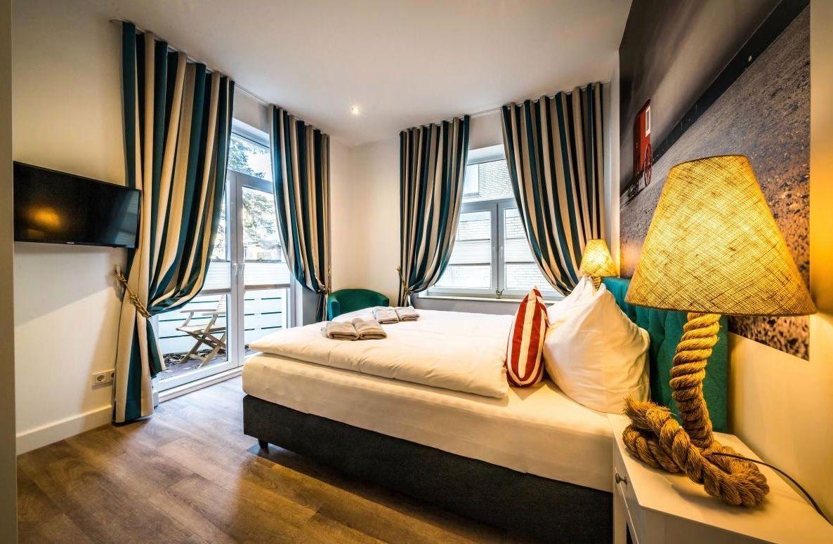 Schlafzimmer mit Bett, TV und Balkon. Vorhänge und Lampe sind sichtbar.