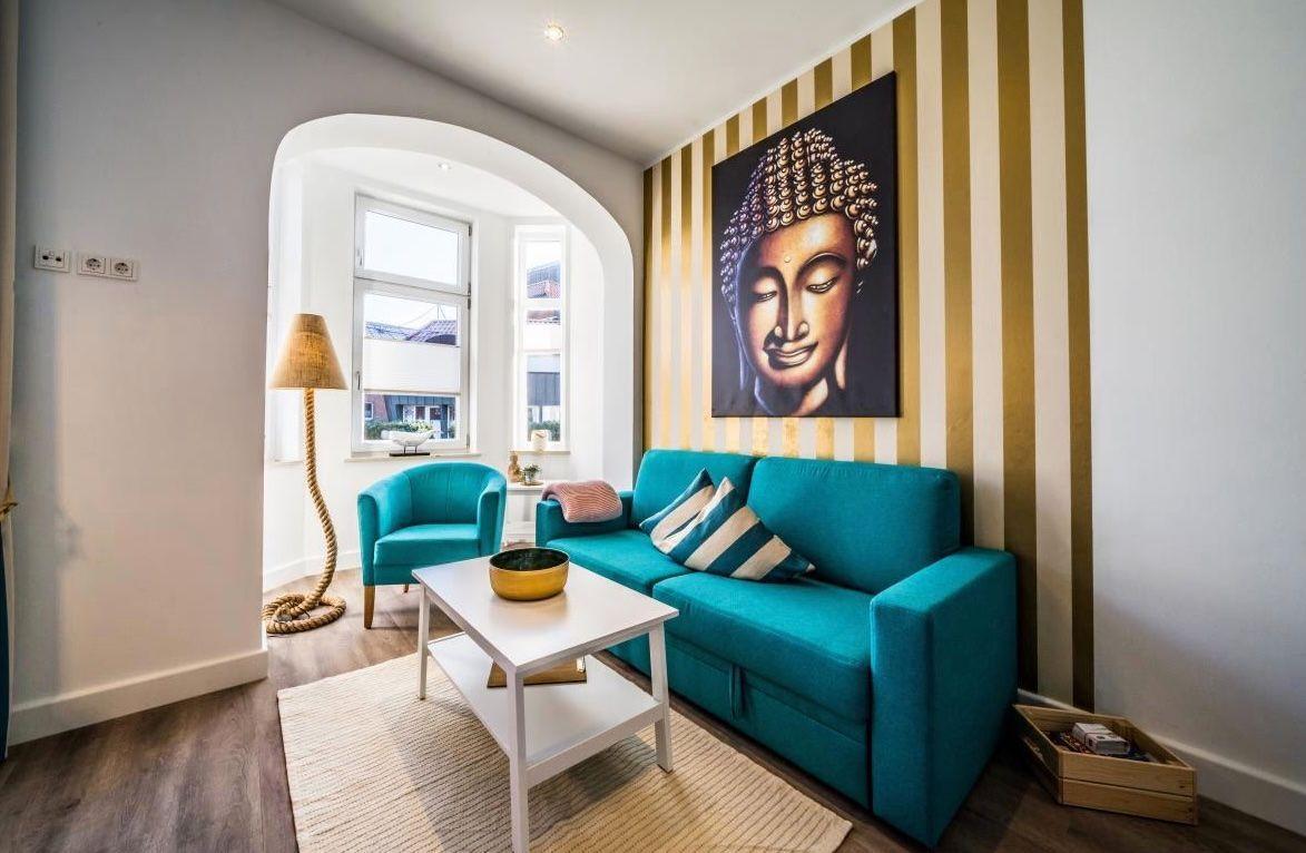 Ein Wohnzimmer mit türkisfarbenem Sofa, Buddha-Bild und Streifenwand.