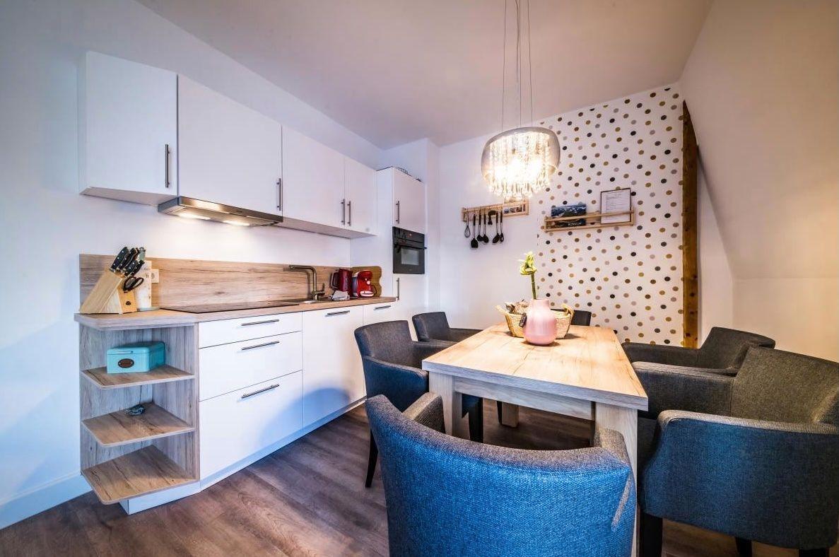 Küche mit Essbereich, Holztisch und Stühlen, weiße Schränke und Holzoberfläche.