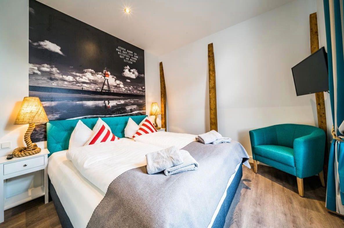 Schlafzimmer mit Bett, Sessel und Wandbild mit Leuchtturm.