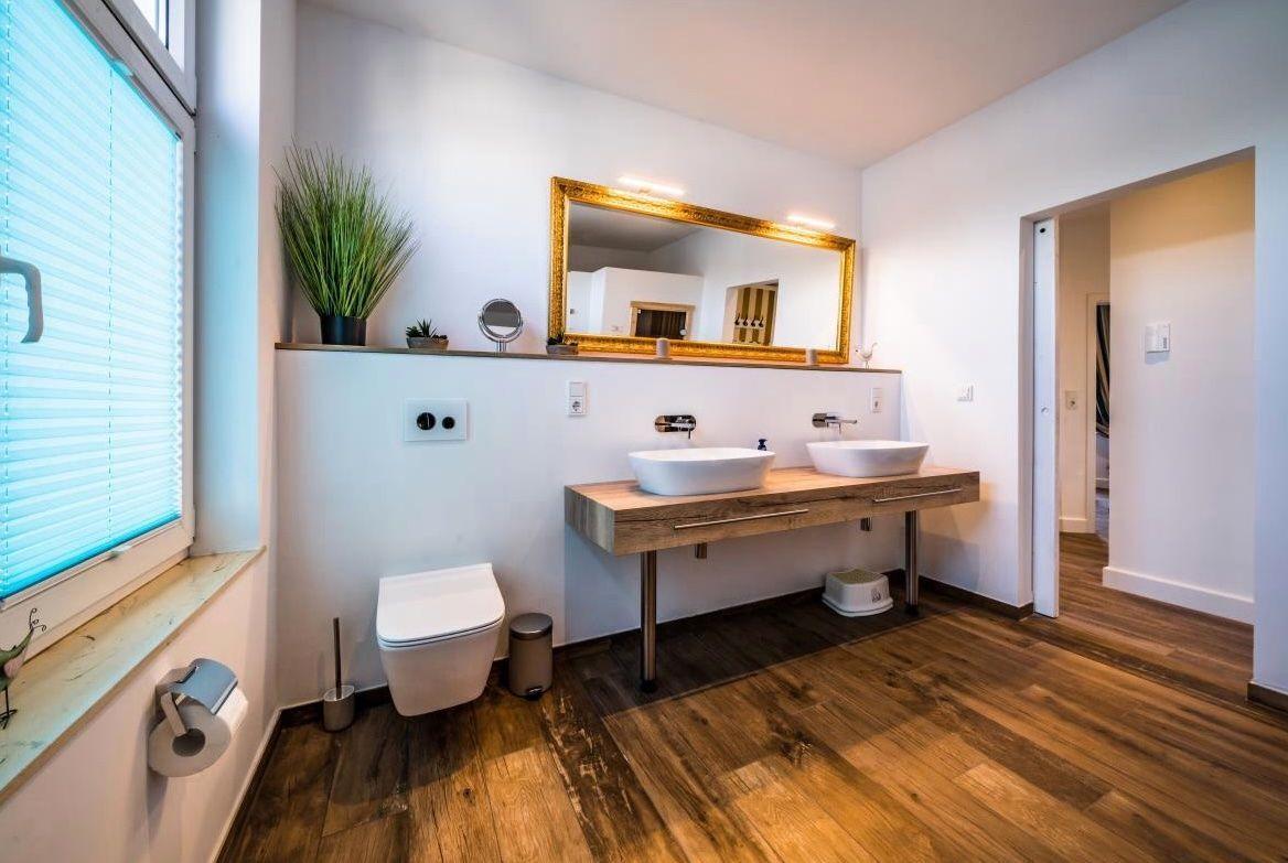 Badezimmer mit Doppelwaschbecken, Spiegel und Holzboden.