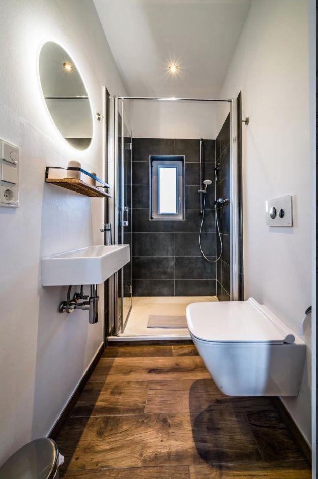 Badezimmer mit Dusche, Waschbecken und Toilette. Holzfußboden und runder Spiegel.