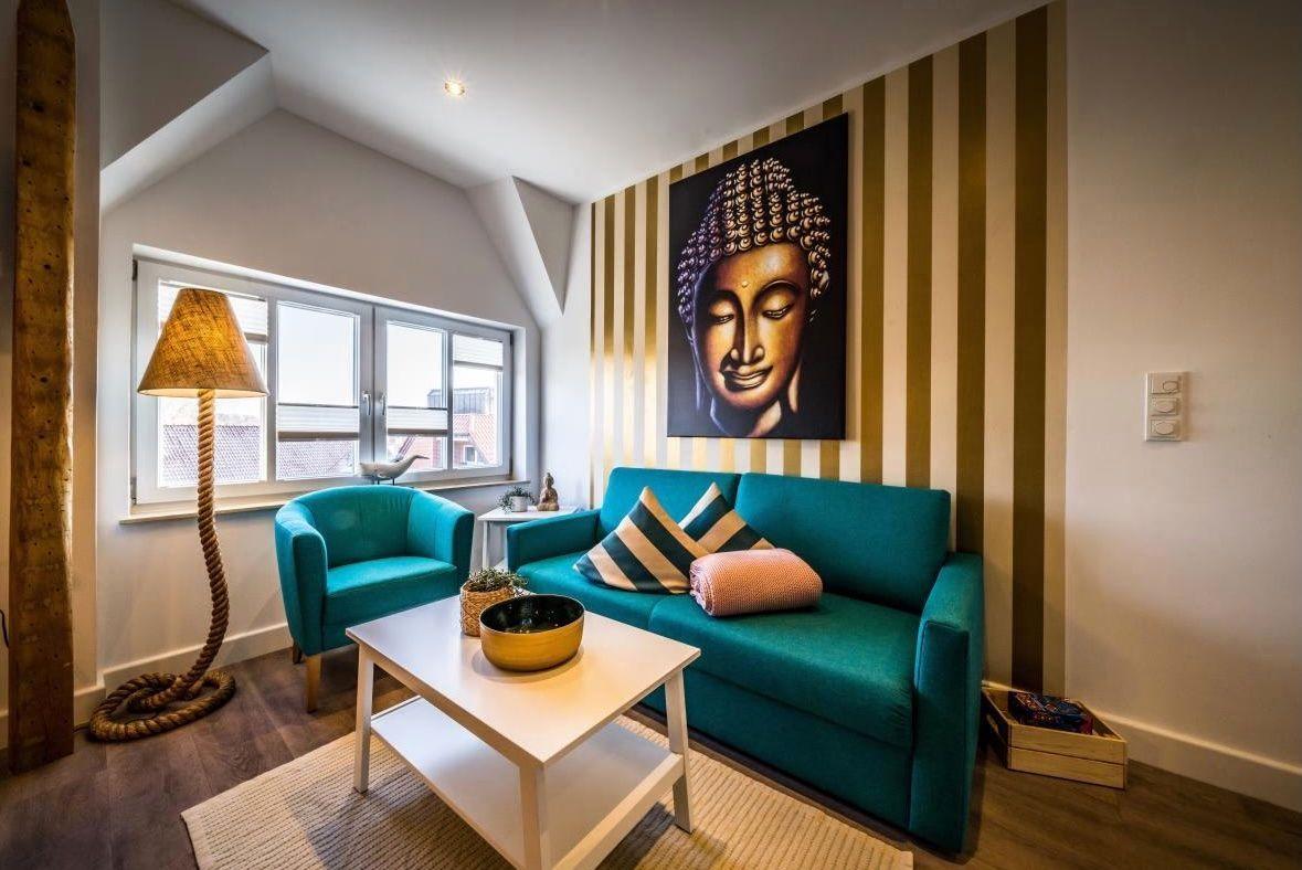 Ein Wohnzimmer mit türkisfarbenem Sofa, einem Buddha-Bild und gestreifter Wand.