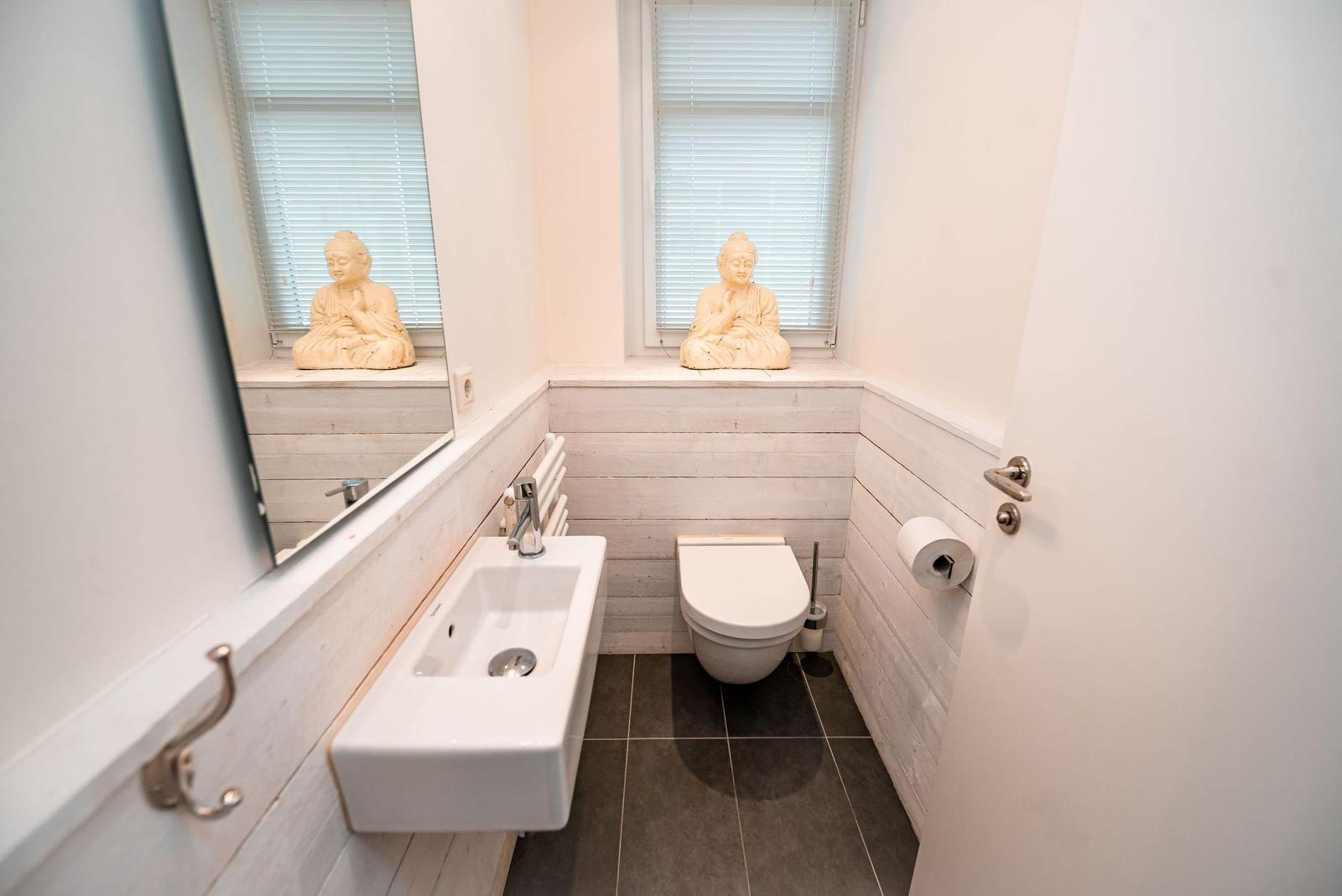 Badezimmer mit Waschbecken, Toilette und Buddha-Statue auf Fensterbank.