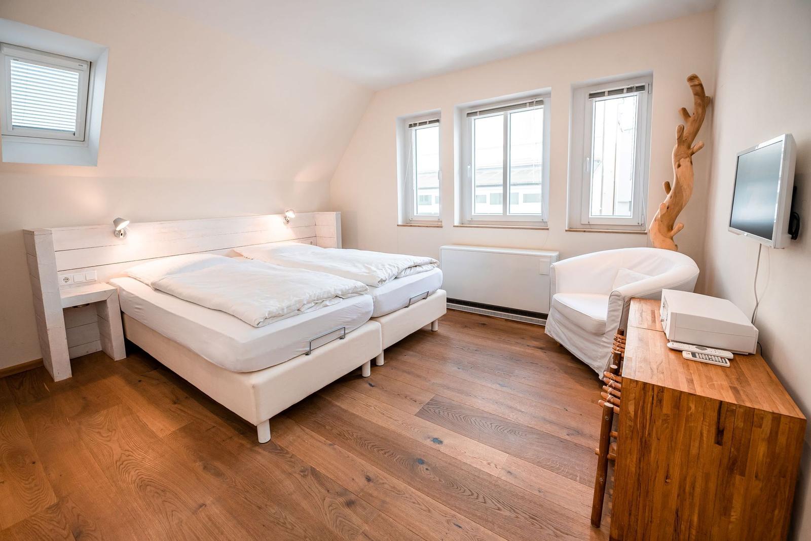Schlafzimmer mit Doppelbett, Holzboden und Fenstern.
