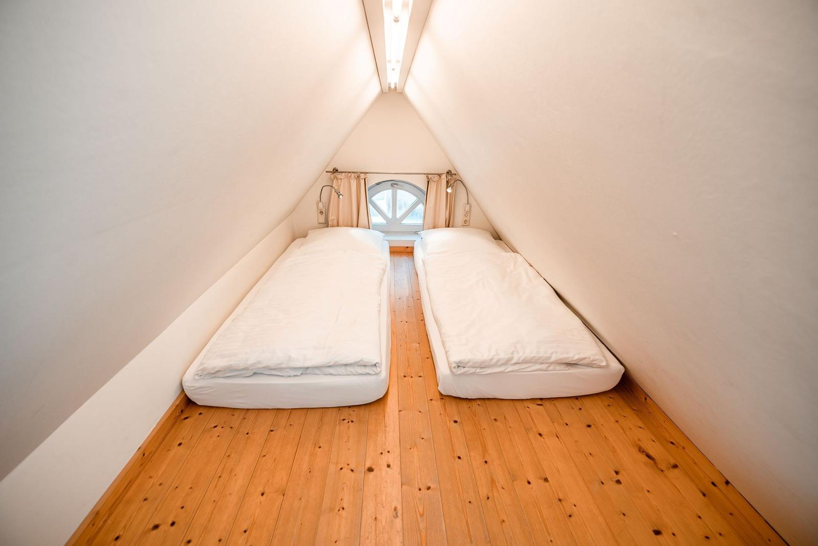 Zwei Betten in einem Dachzimmer mit Holzboden und Fenster