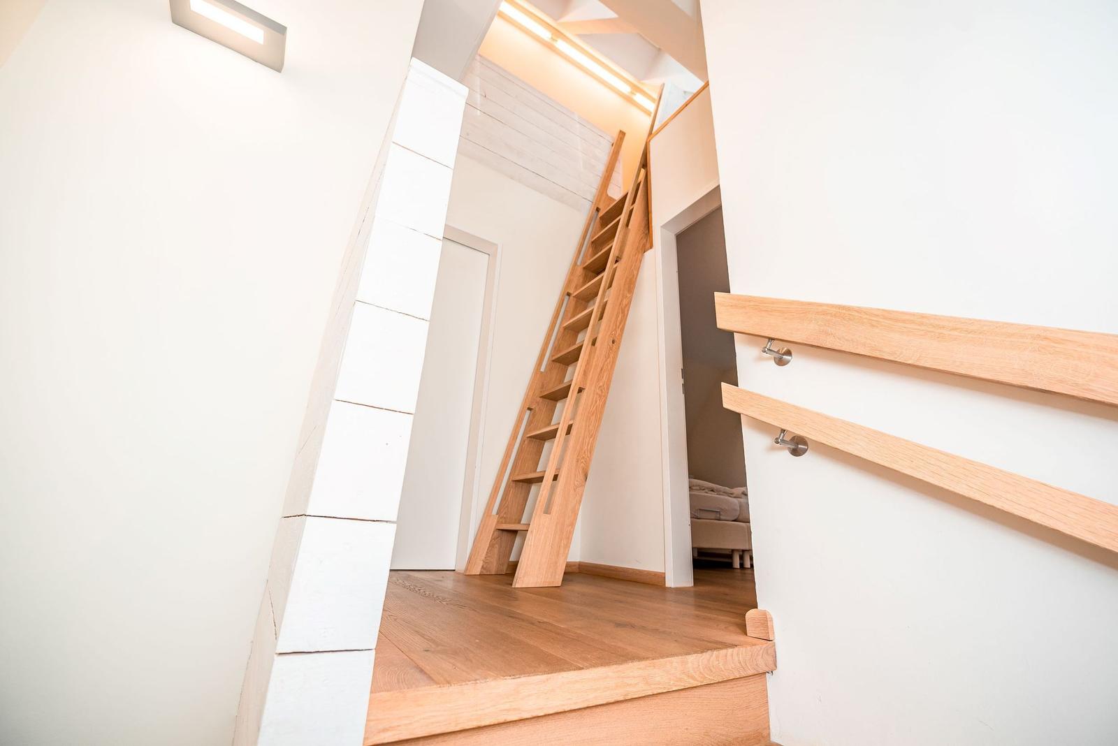 Holztreppe führt zu einer oberen Etage mit Schlafzimmer. Moderne Beleuchtung und Holzboden.
