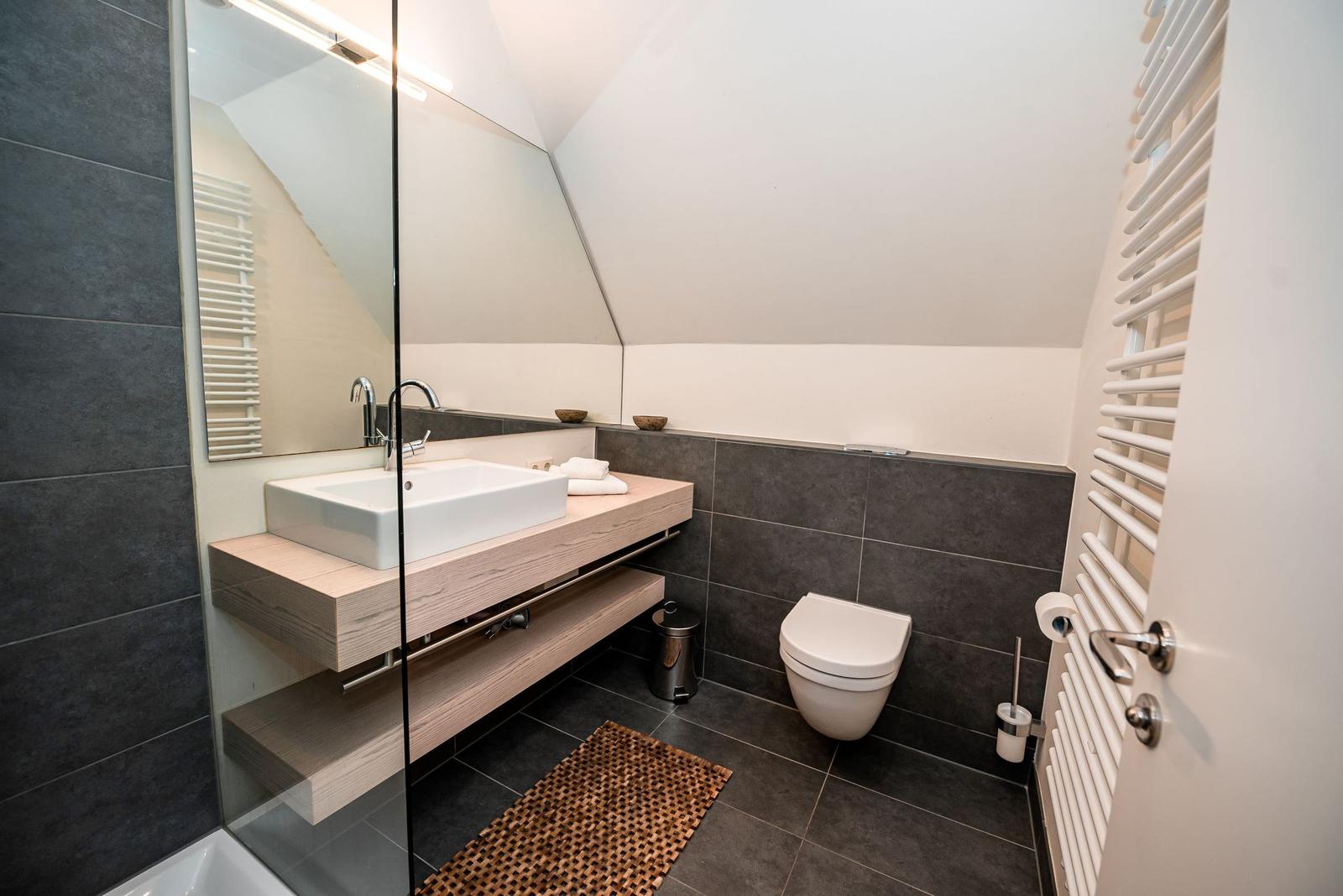 Badezimmer mit Dusche, Waschbecken und Toilette. Schwarze Fliesen und Holzoberflächen.
