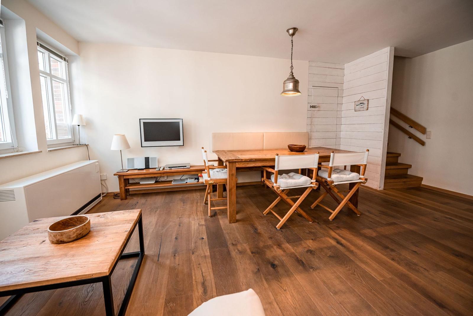 Wohn- und Essbereich mit Holzboden, TV und Tisch mit Stühlen.