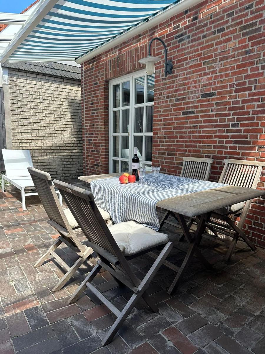 Terrasse mit Holztisch, Stühlen und Sonnenschutz. Tisch gedeckt mit Wein und Obst.