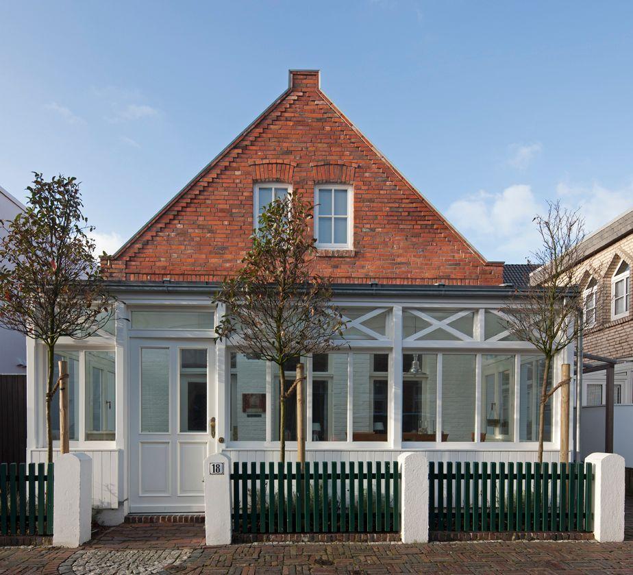 Haus mit rotem Ziegeldach und weißem Vordach. Grün gestrichener Zaun vor der Eingangstür.