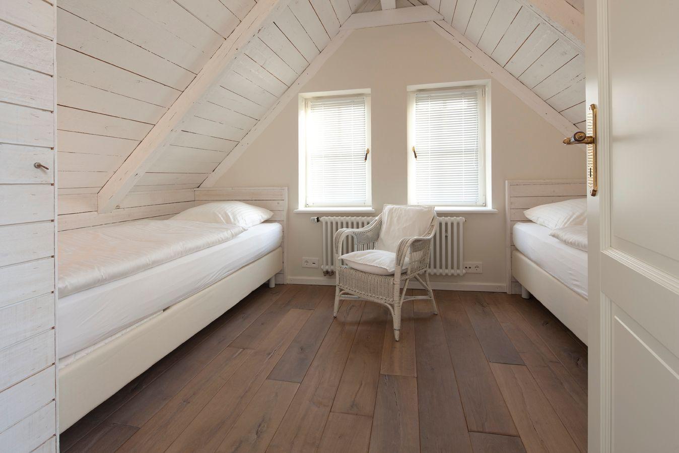Zimmer mit zwei Betten, Holzboden und Dachschräge mit Fenstern.