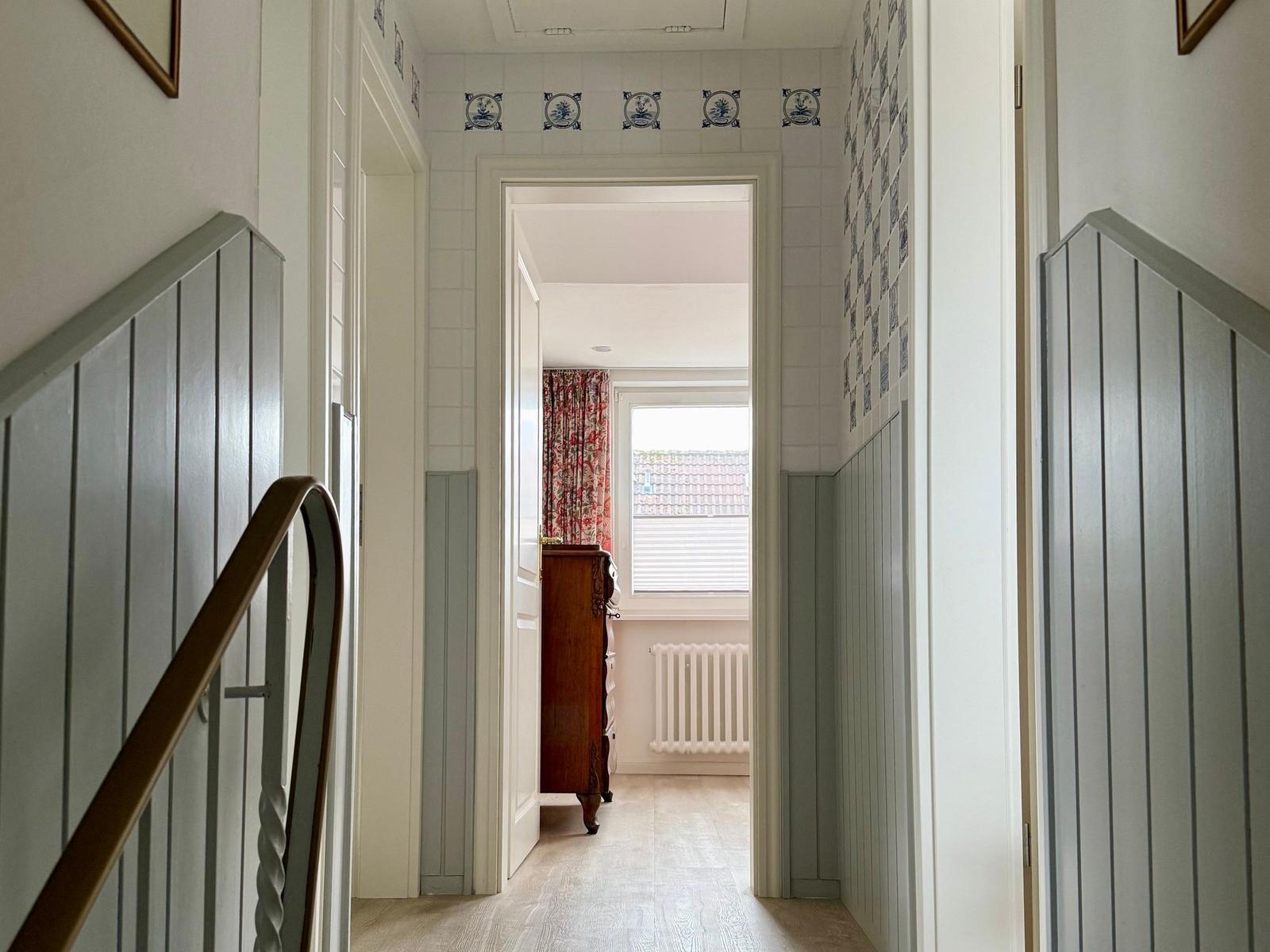 Flur mit Holzboden, blau-weißen Fliesen und Holzgeländer.