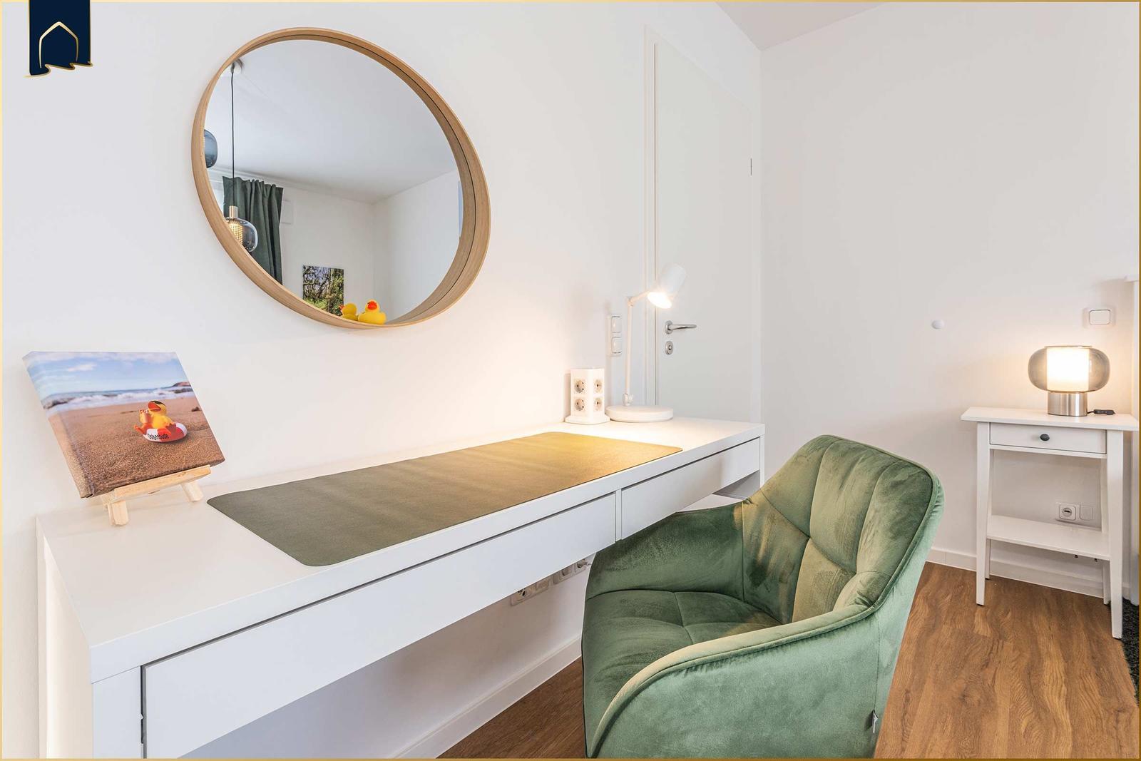 Schreibtisch mit grünem Sessel und runden Spiegel an der Wand.