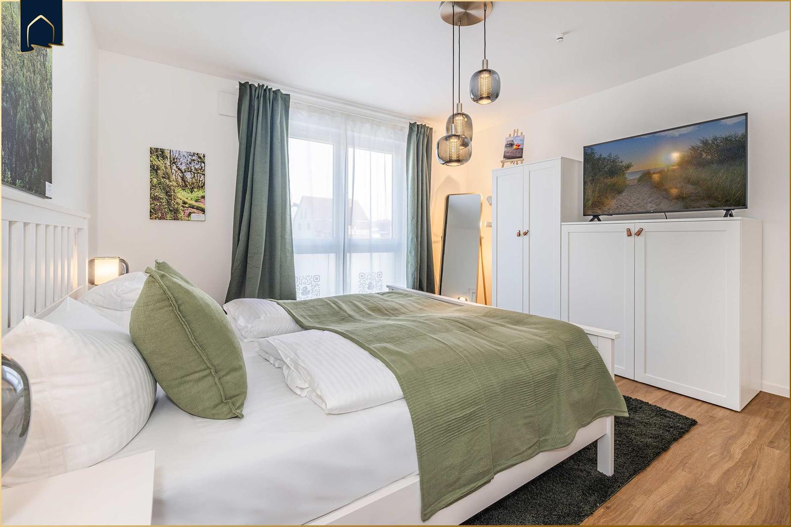 Schlafzimmer mit Bett, Fernseher und Fenster.
