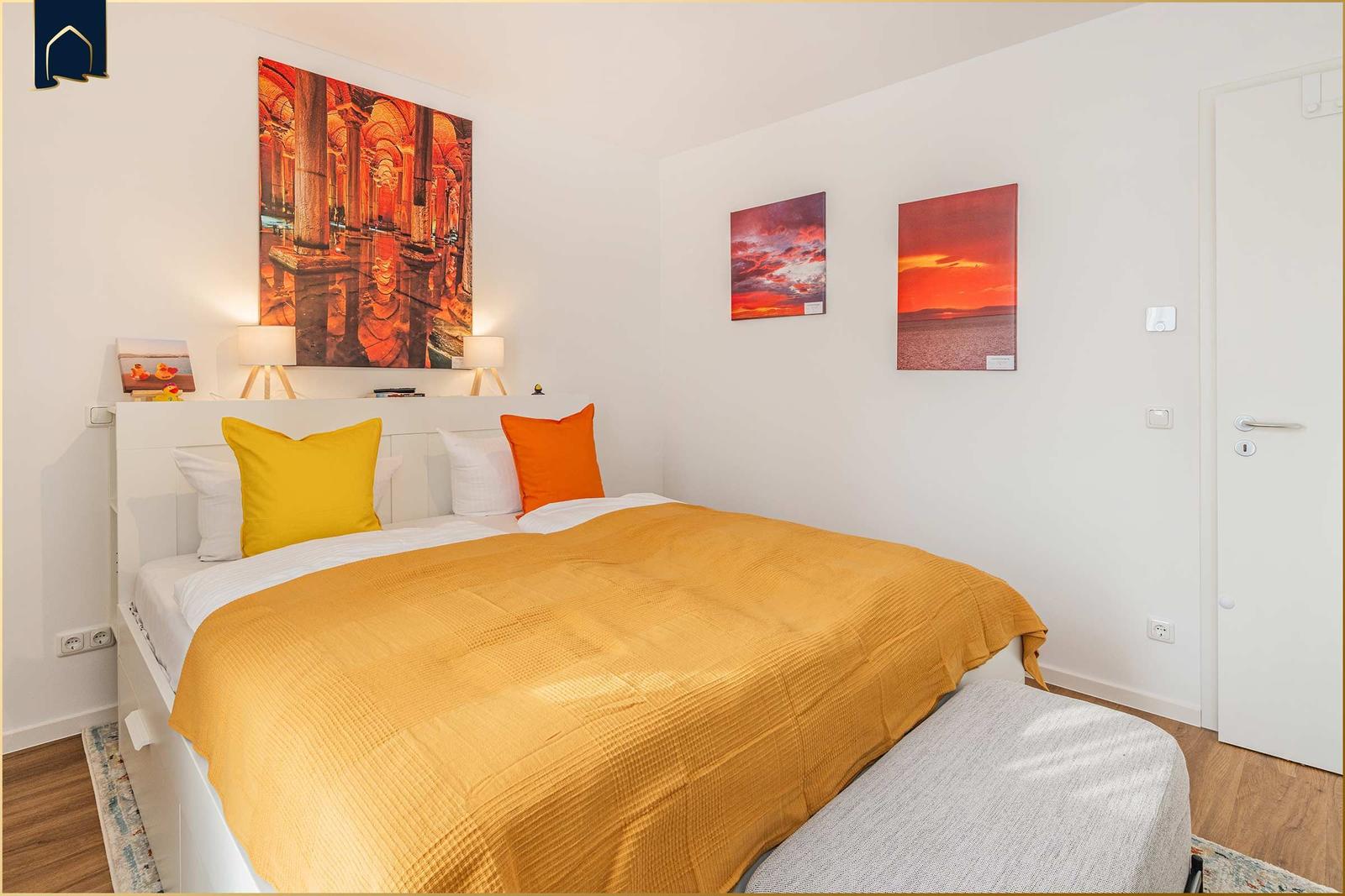 Schlafzimmer mit Bett, Kissen und Wandbildern.