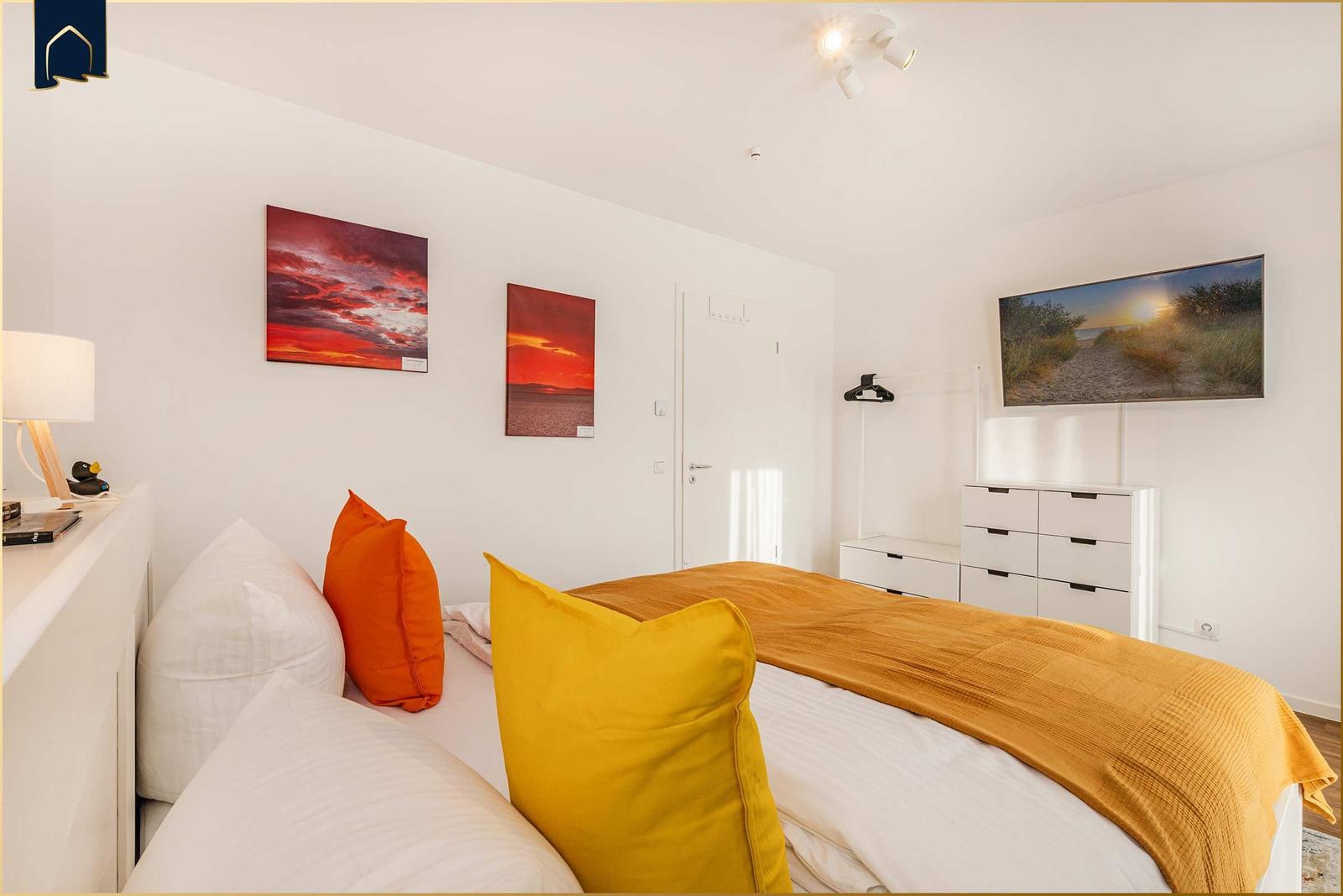 Schlafzimmer mit Bett, Wandbildern und Schrank.