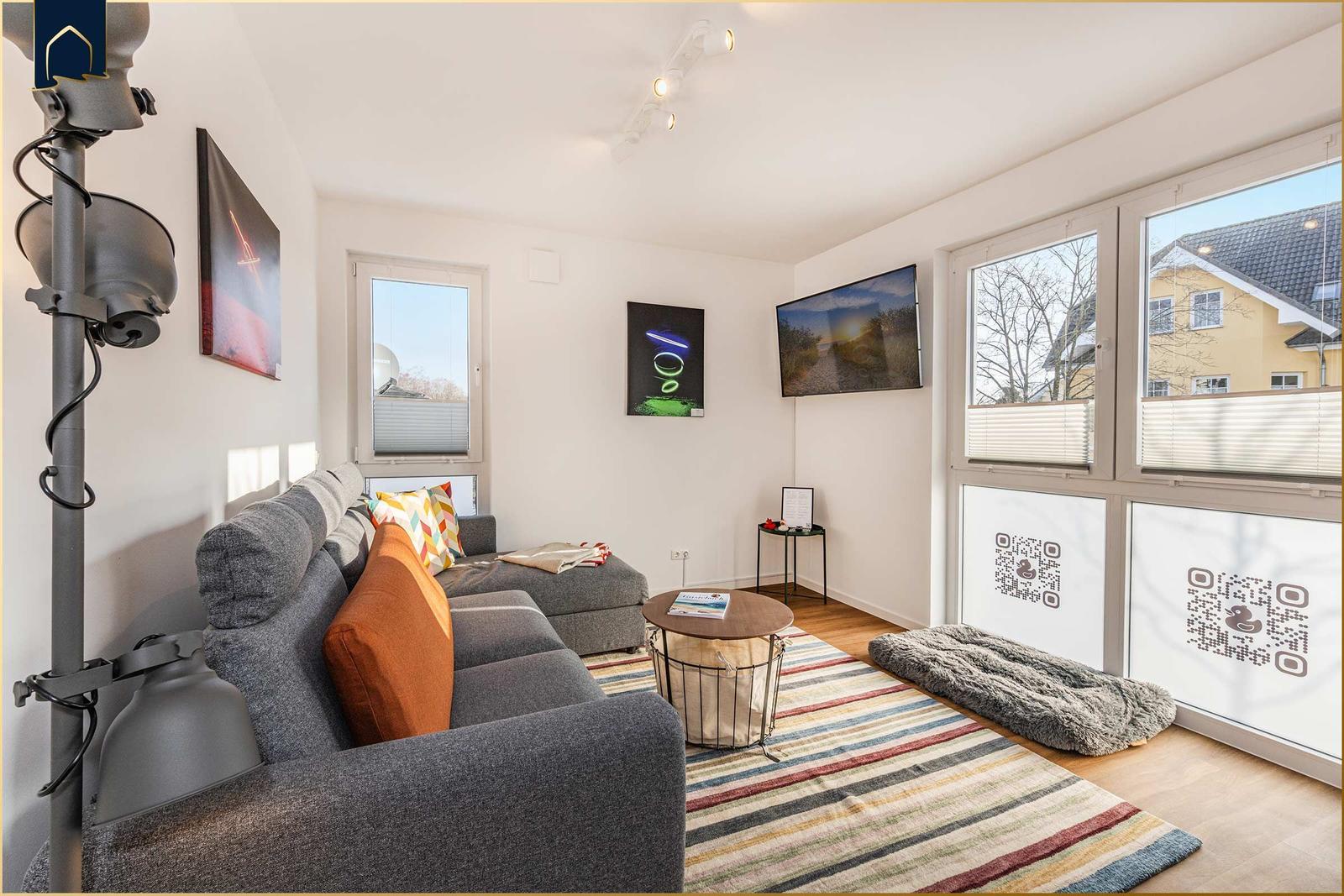 Wohnzimmer mit Sofa, Fernseher und großen Fenstern.