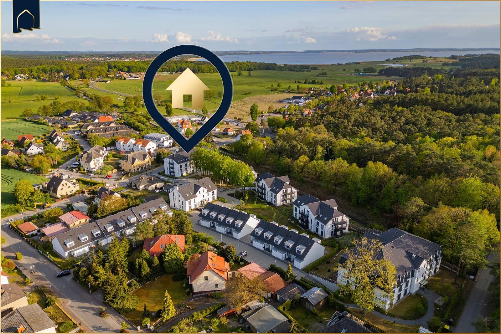 Luftbild einer Wohnsiedlung mit Wald und See im Hintergrund.