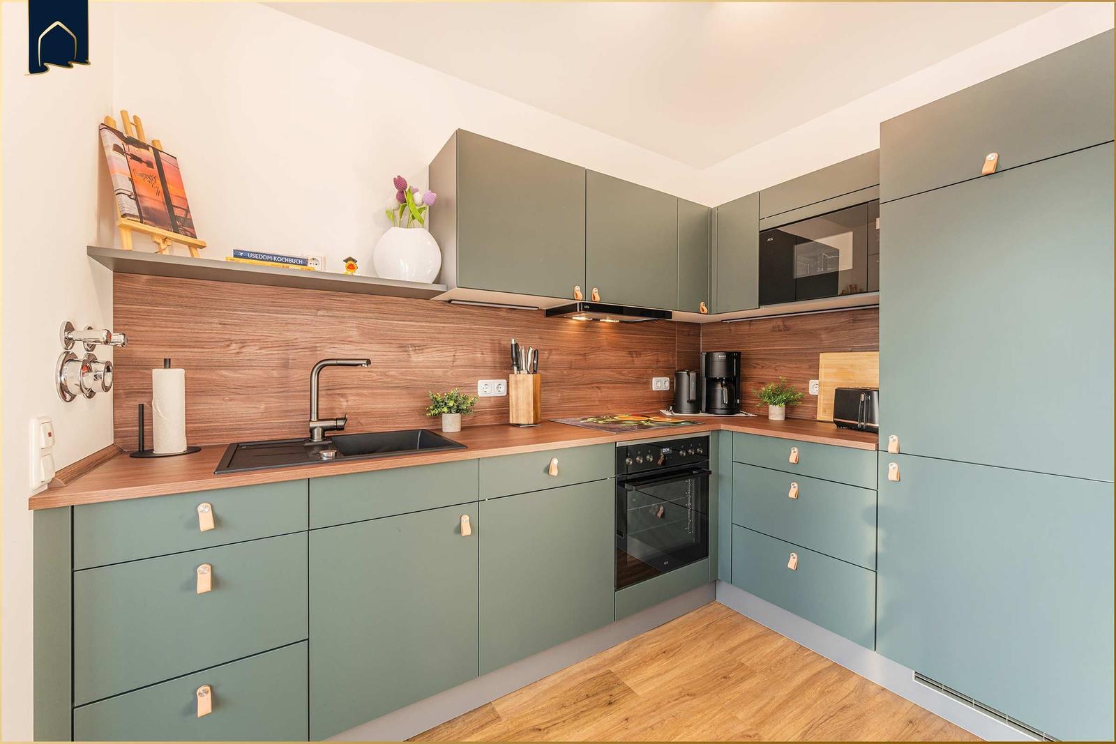 Moderne Küche mit grünen Schränken, Holzoberfläche und integriertem Backofen.