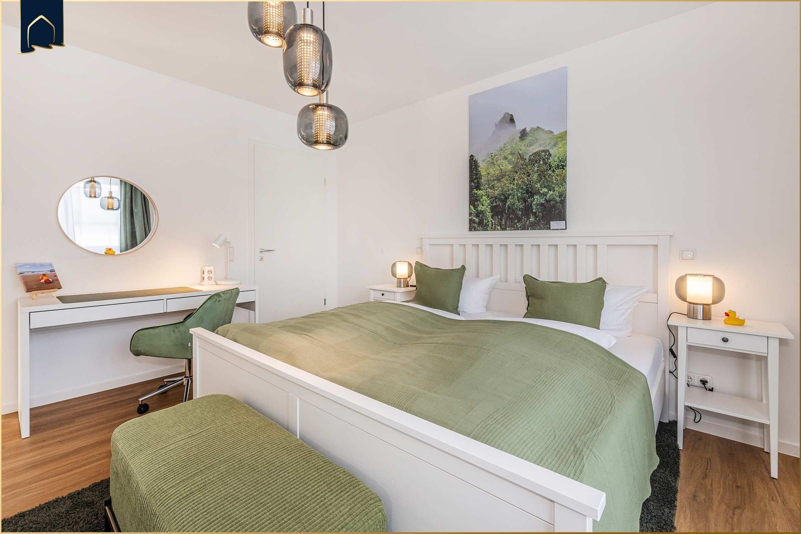 Schlafzimmer mit Bett, Schreibtisch und Wandbild.