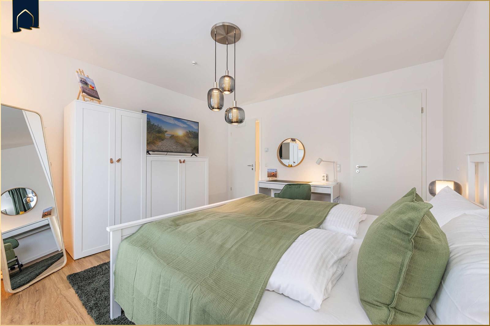Schlafzimmer mit Bett, Kleiderschrank, TV und Schreibtisch.
