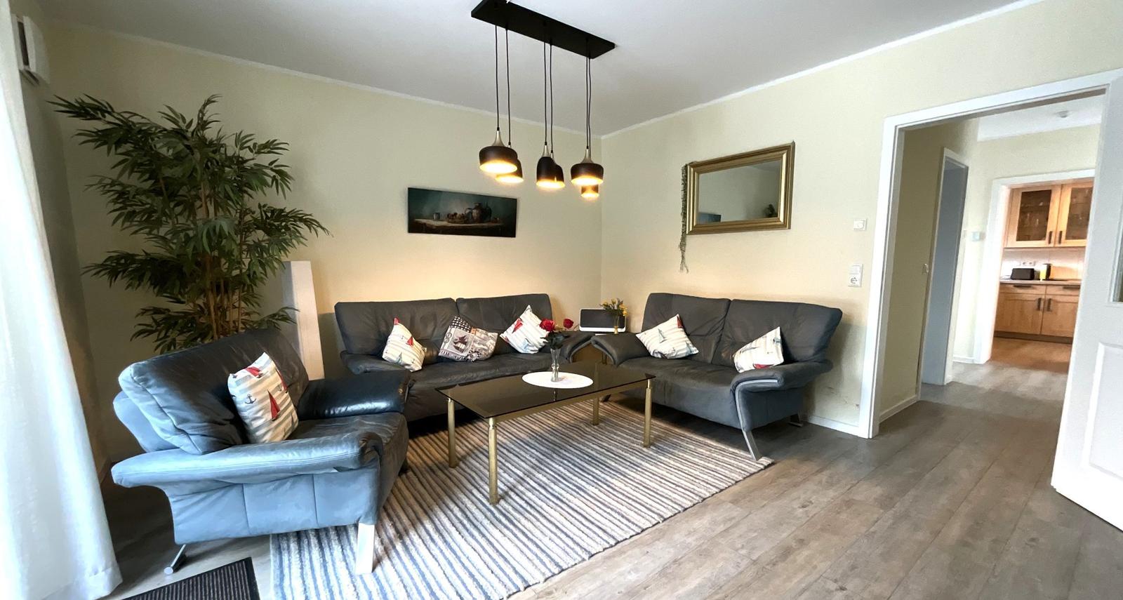 Wohnzimmer mit zwei Sofas, Sitzbank und Couchtisch. Küche im Hintergrund.