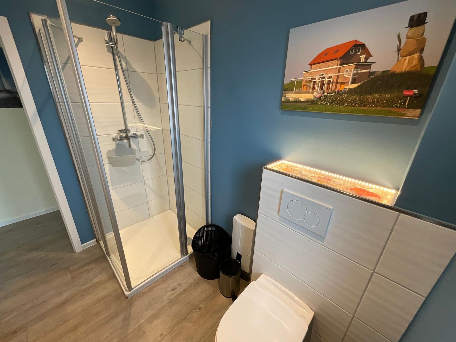 Dusche mit Glaswand, Toilette und Wandbild mit Haus.
