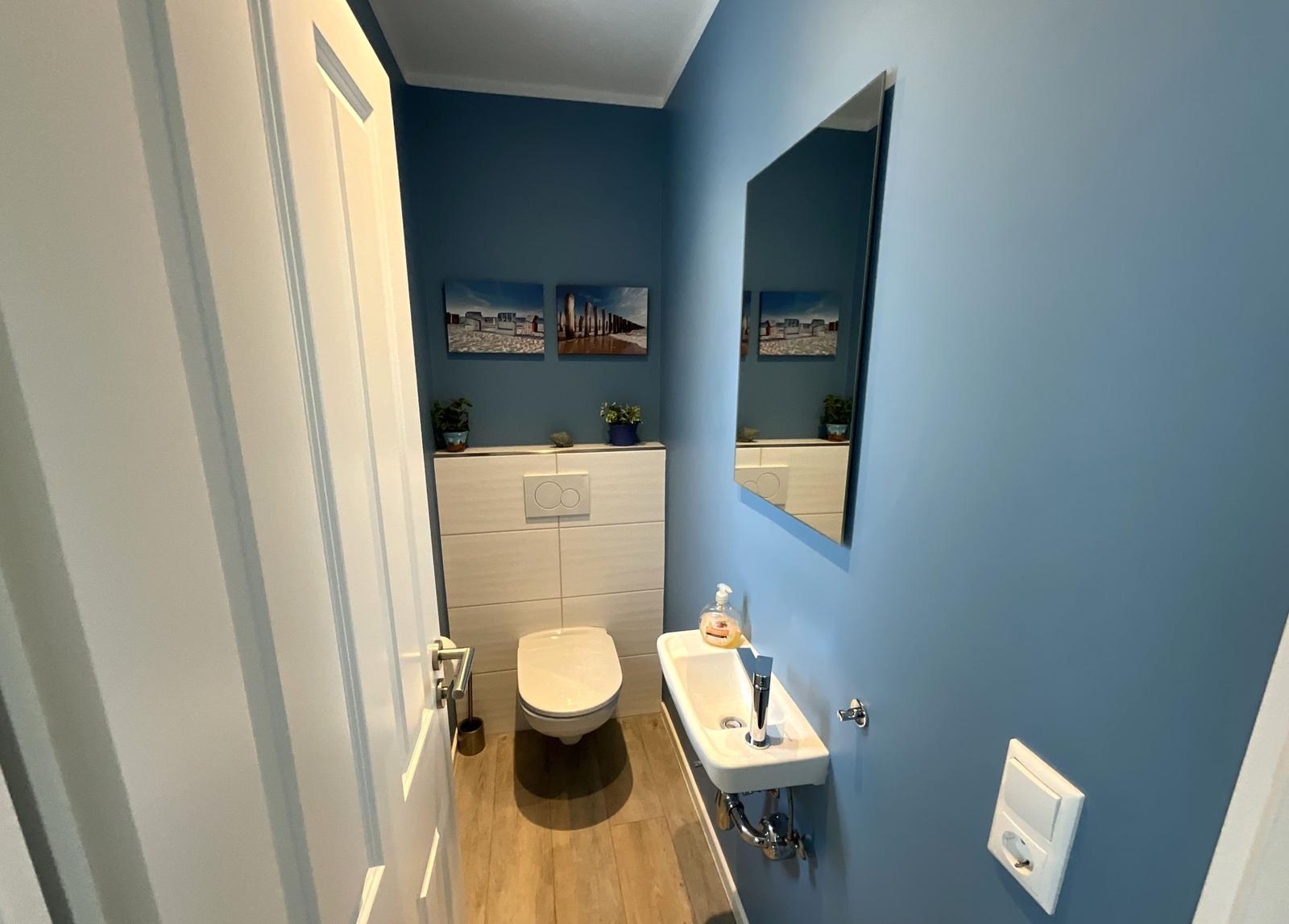 Badezimmer mit Toilette, Waschbecken und Spiegel an blauen Wänden.