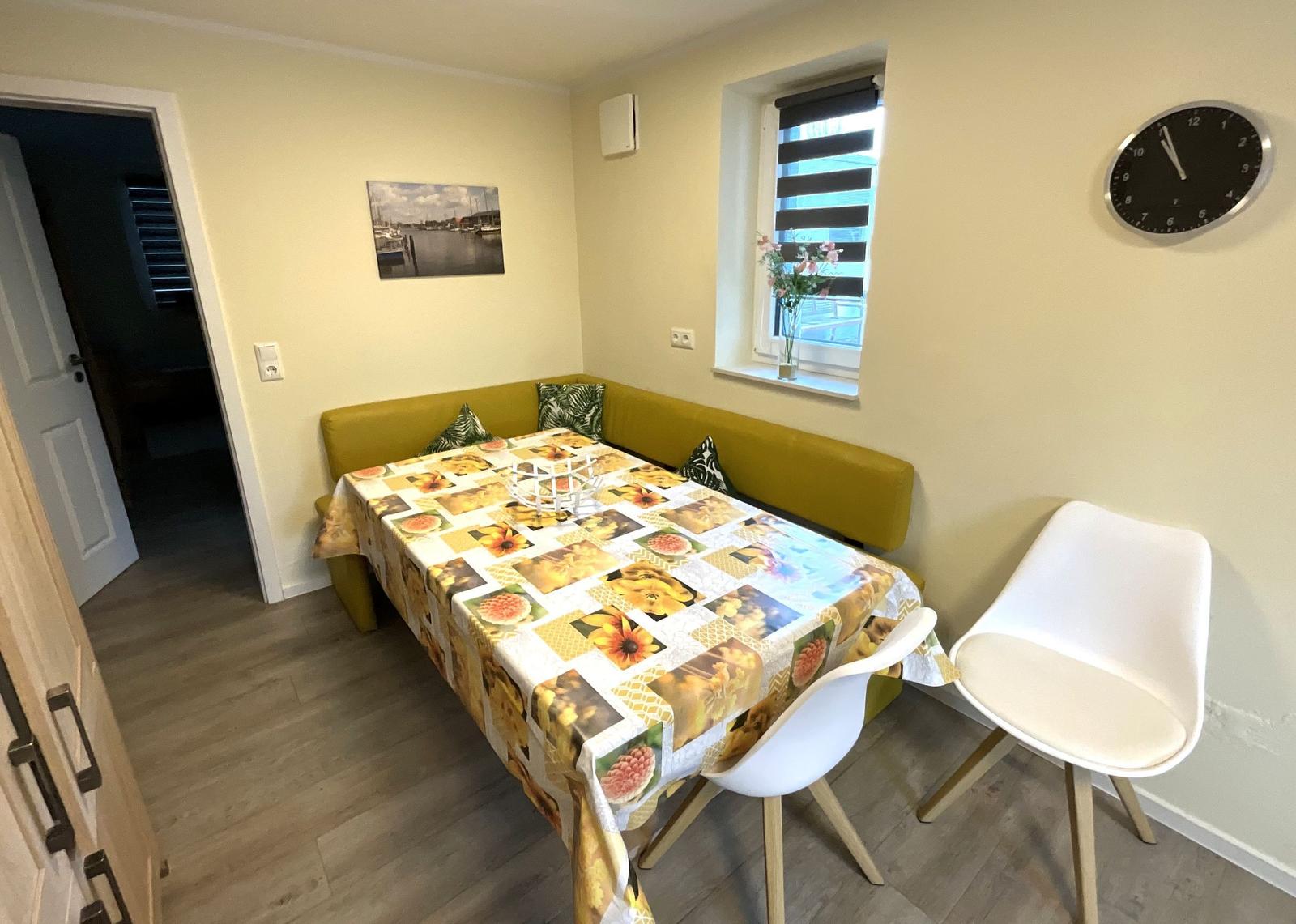 Essbereich mit grünem Sofa, Tisch mit Tischdecke und zwei weißen Stühlen.