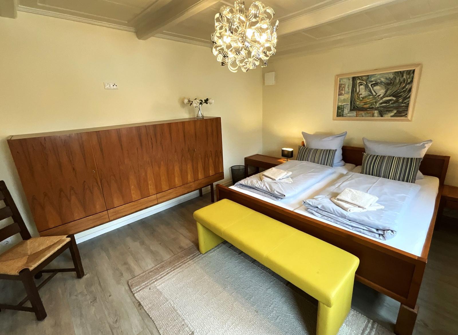 Schlafzimmer mit Doppelbett, Holzschrank und gelber Sitzbank.