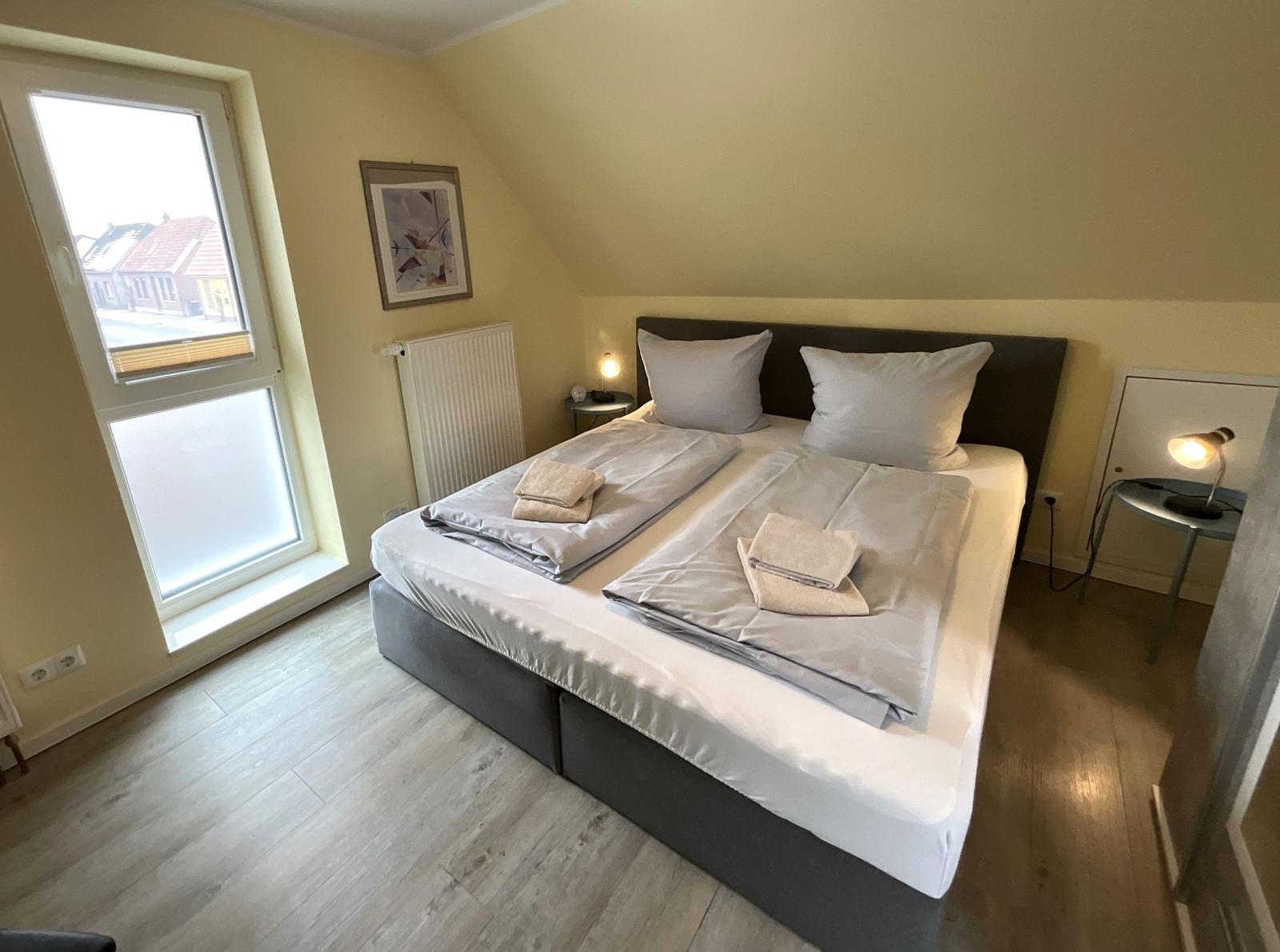 Schlafzimmer mit Doppelbett, Fenster und Nachttischen.