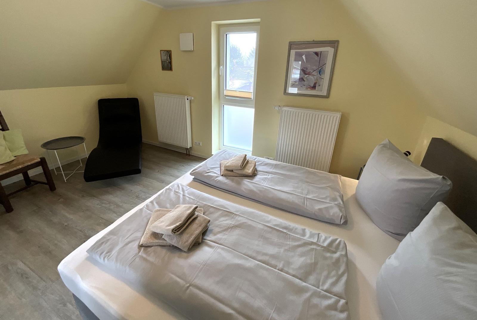 Schlafzimmer mit Doppelbett, Fenster und Sitzgelegenheit.