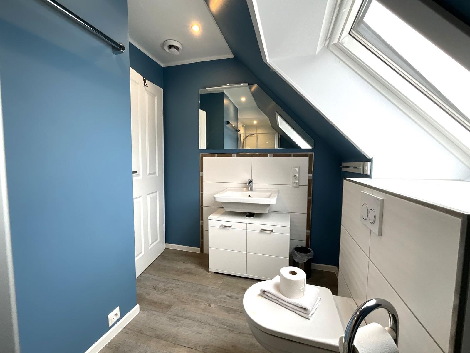 Badezimmer mit Dachschrägen, Waschbecken, Spiegel und Toilette.