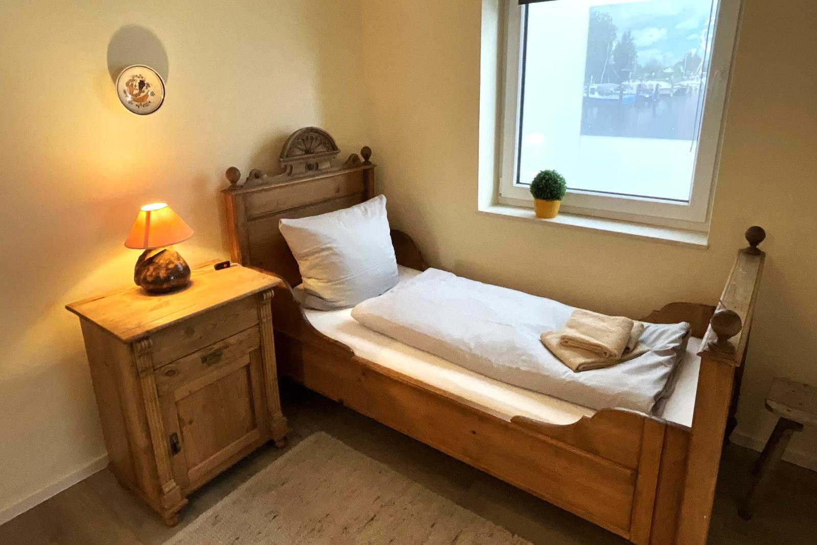Ein Schlafzimmer mit Holzbett, Nachttisch und Fenster mit Blick auf Wasser.