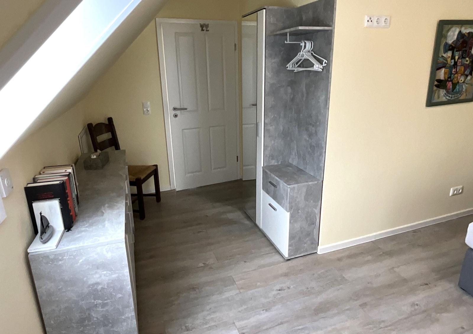 Schlafzimmer mit Dachschrägen, Schrank und Schreibtisch.