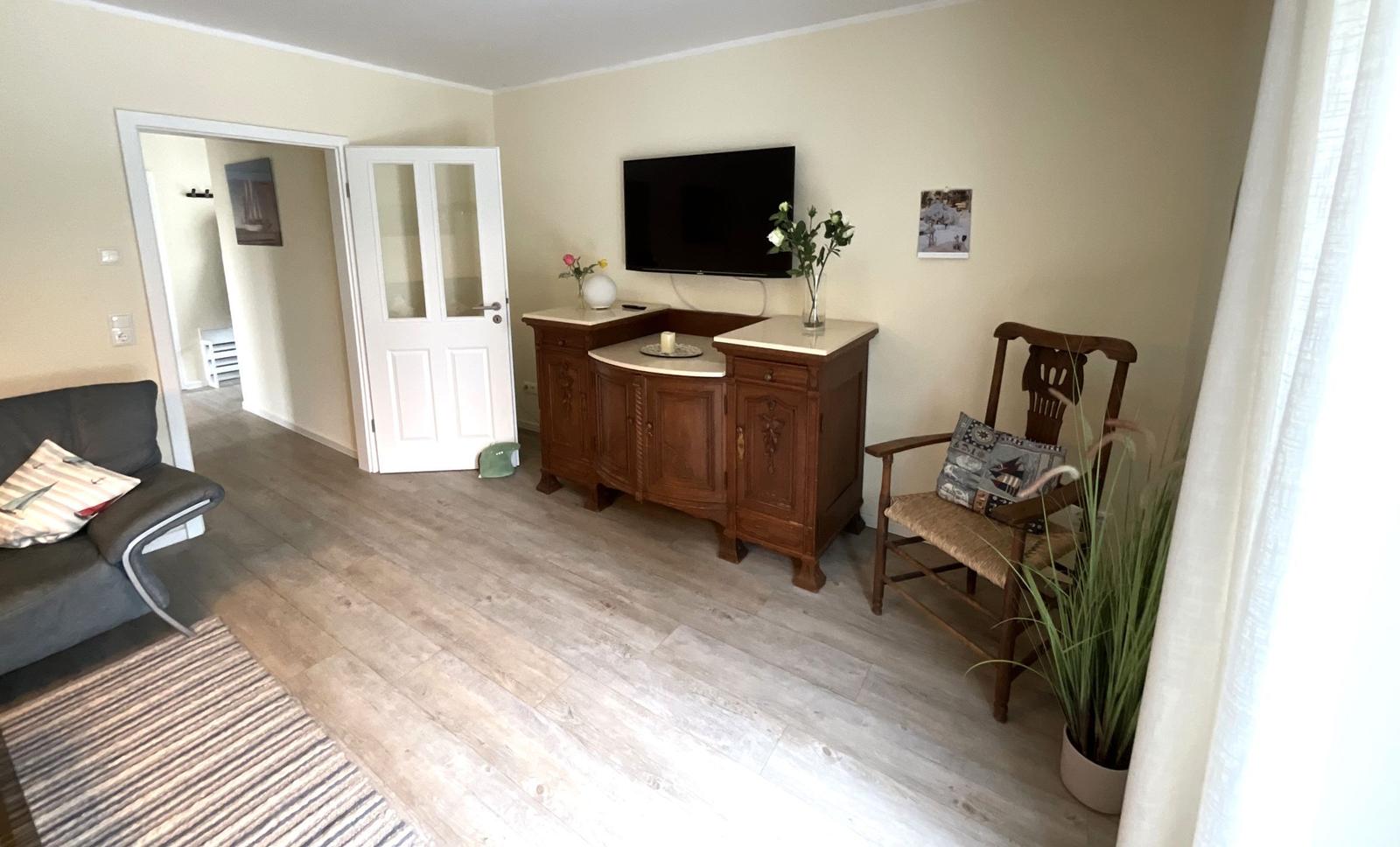 Wohnzimmer mit Sofa, TV-Schrank und Holzstuhl. Holzfußboden und helle Wände.