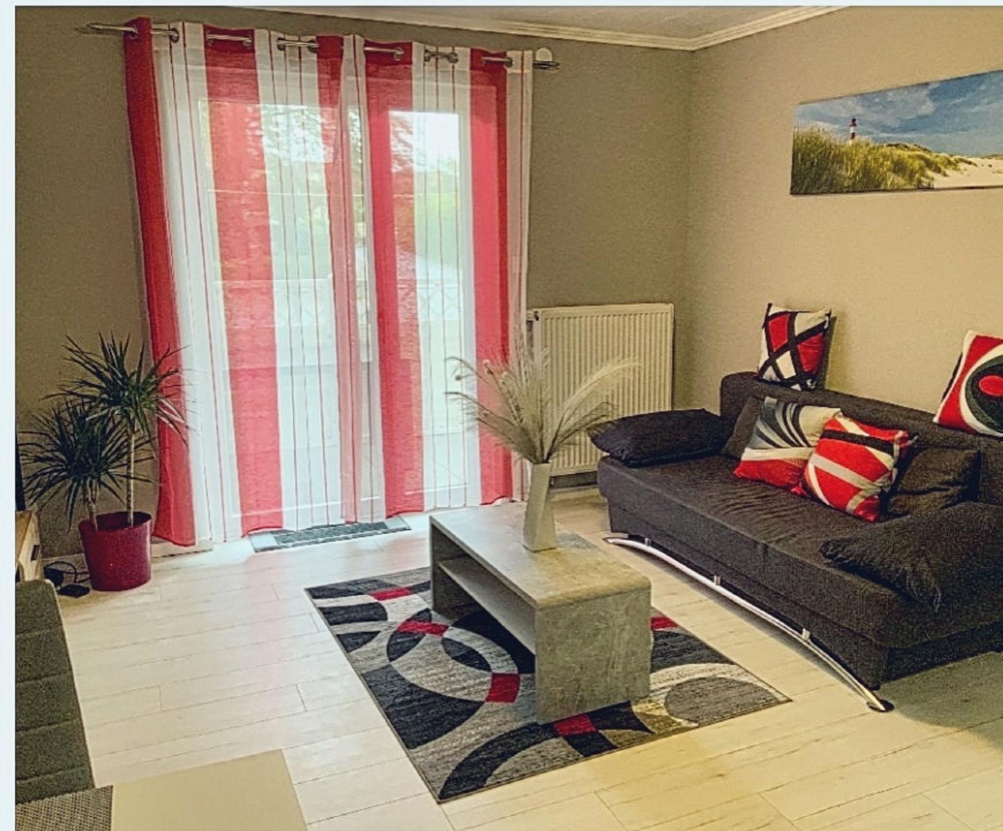 Wohnzimmer mit Sofa, Couchtisch und roten Vorhängen.