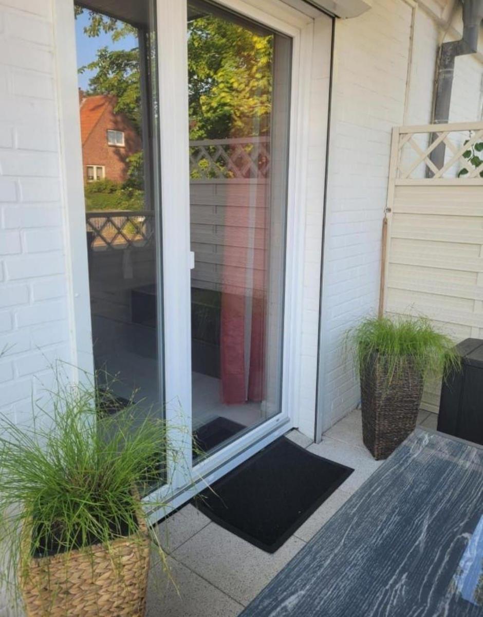 Terrasse mit Glastür, Pflanzen und Bodenmatte. Blick auf Garten und Nachbarhaus.