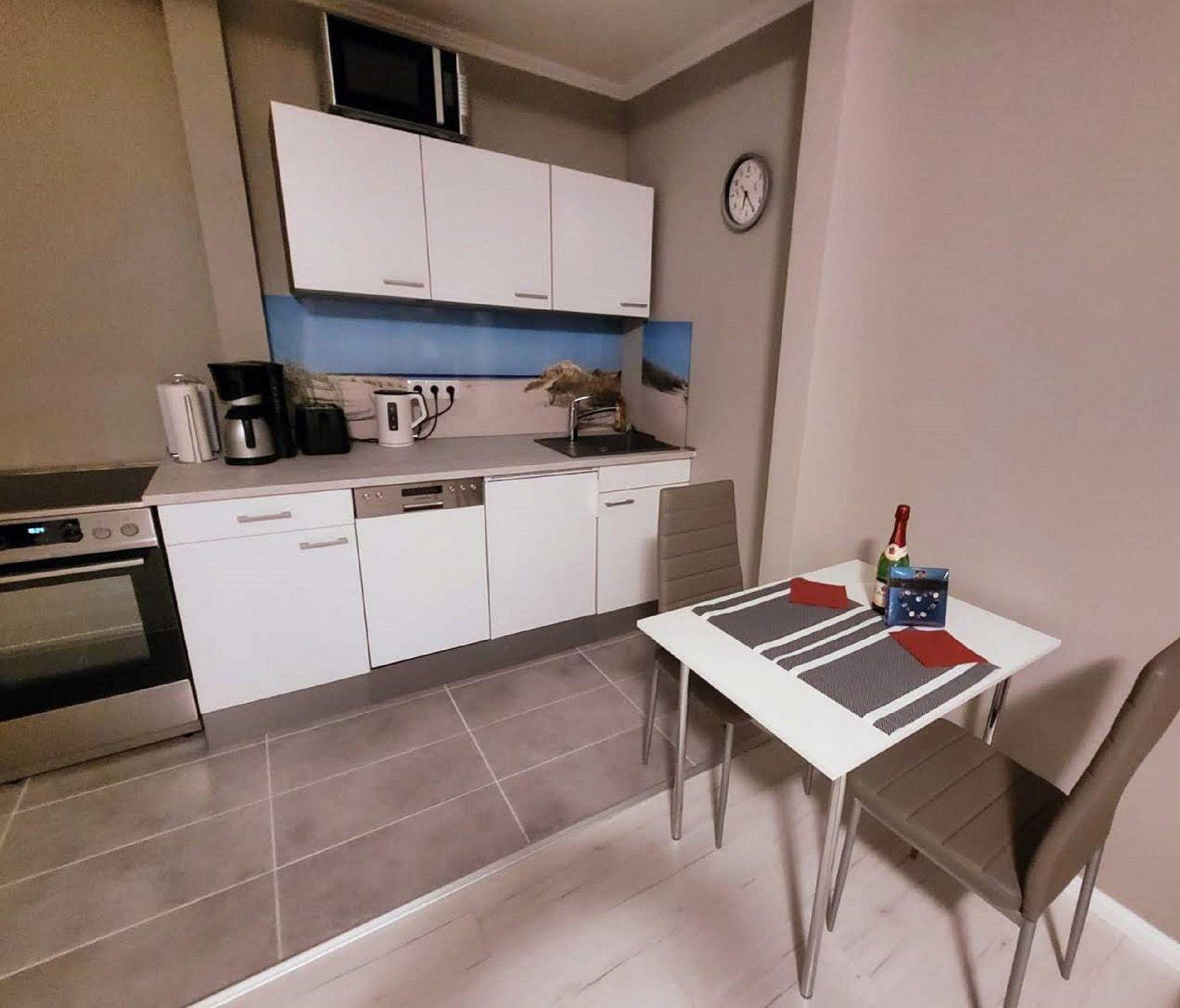 Küche mit Essbereich, weißen Schränken und Tisch mit zwei Stühlen.