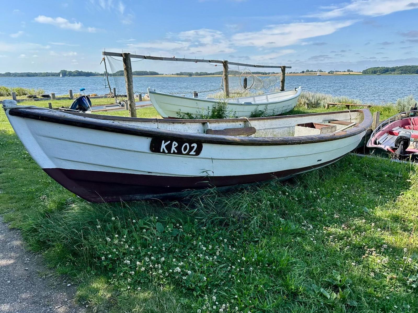 Weiße Boot mit Kennzeichnung KR 02 steht auf Gras am Wasser.