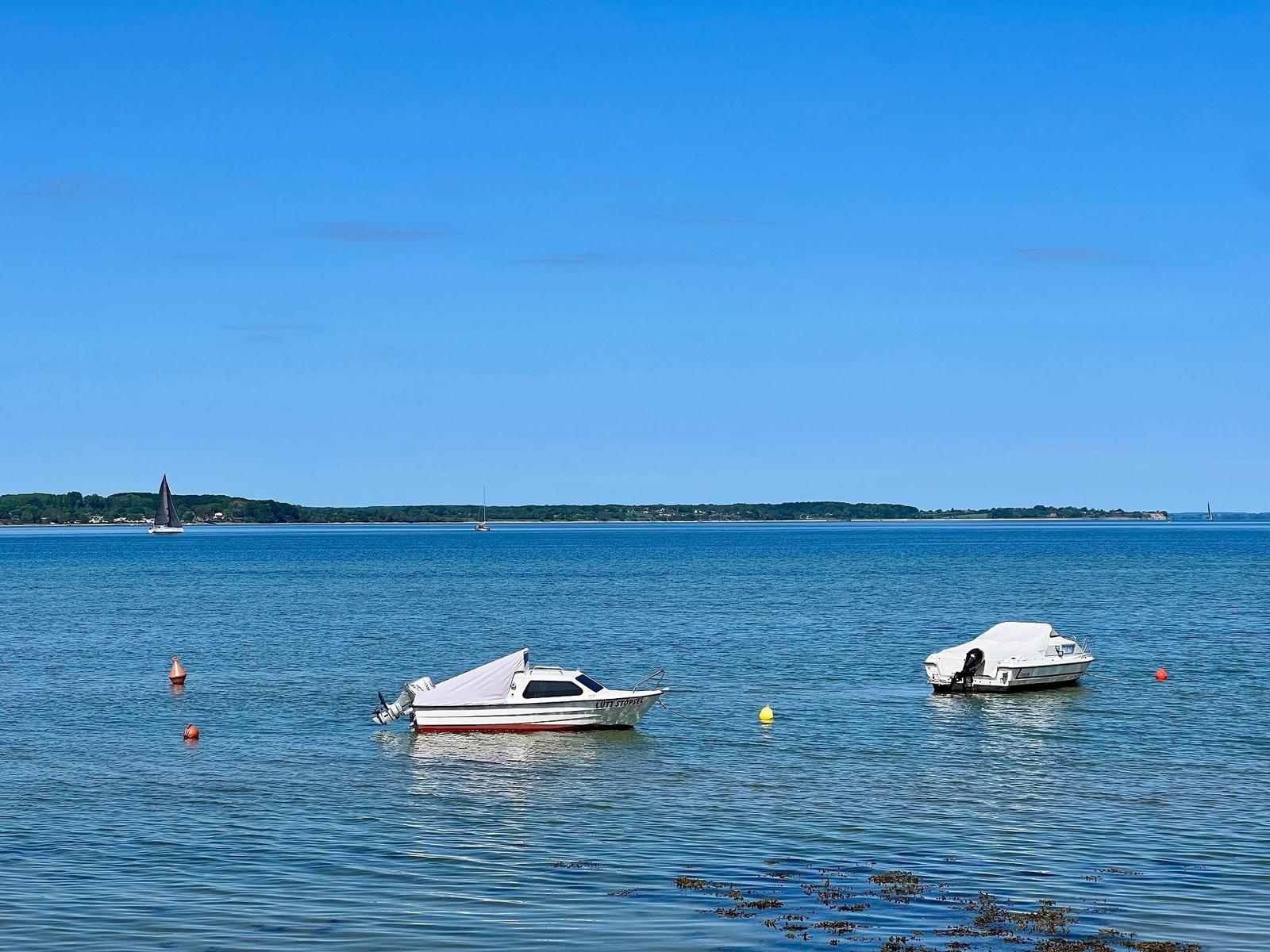 Zwei Motorboote und ein Segelboot auf ruhigem Wasser unter blauem Himmel.