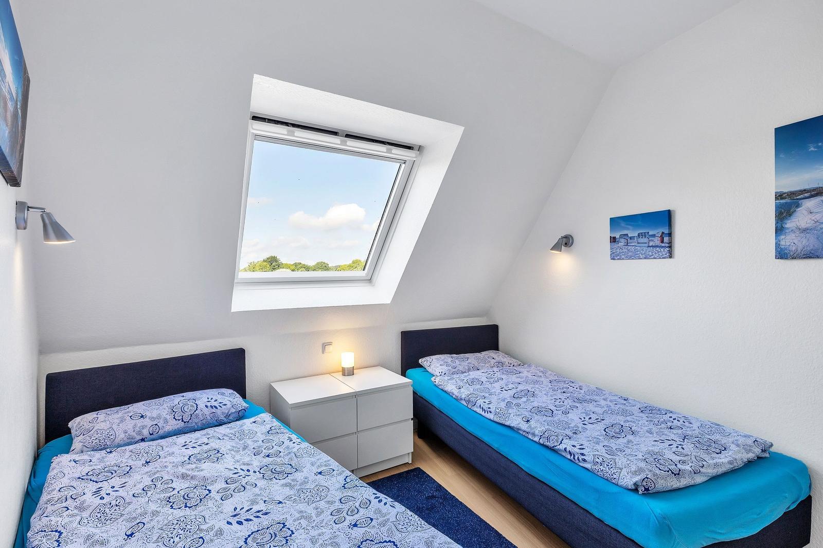 Zwei Einzelbetten mit blauer Bettwäsche, Dachfenster und Wandlampen.