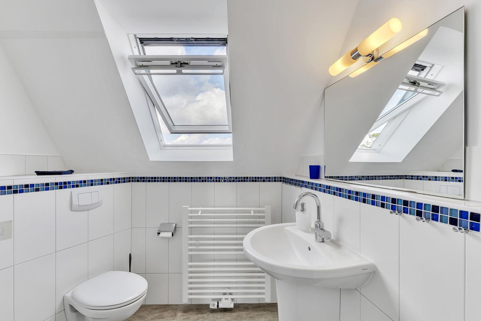 Badezimmer mit Dachfenster, Waschbecken und Toilette. Blaue Fliesenleiste.