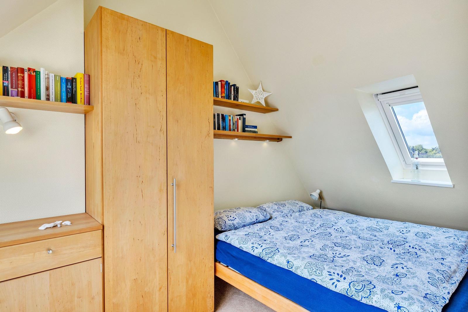 Schlafzimmer mit Dachschräge, Bett, Kleiderschrank und Dachfenster.