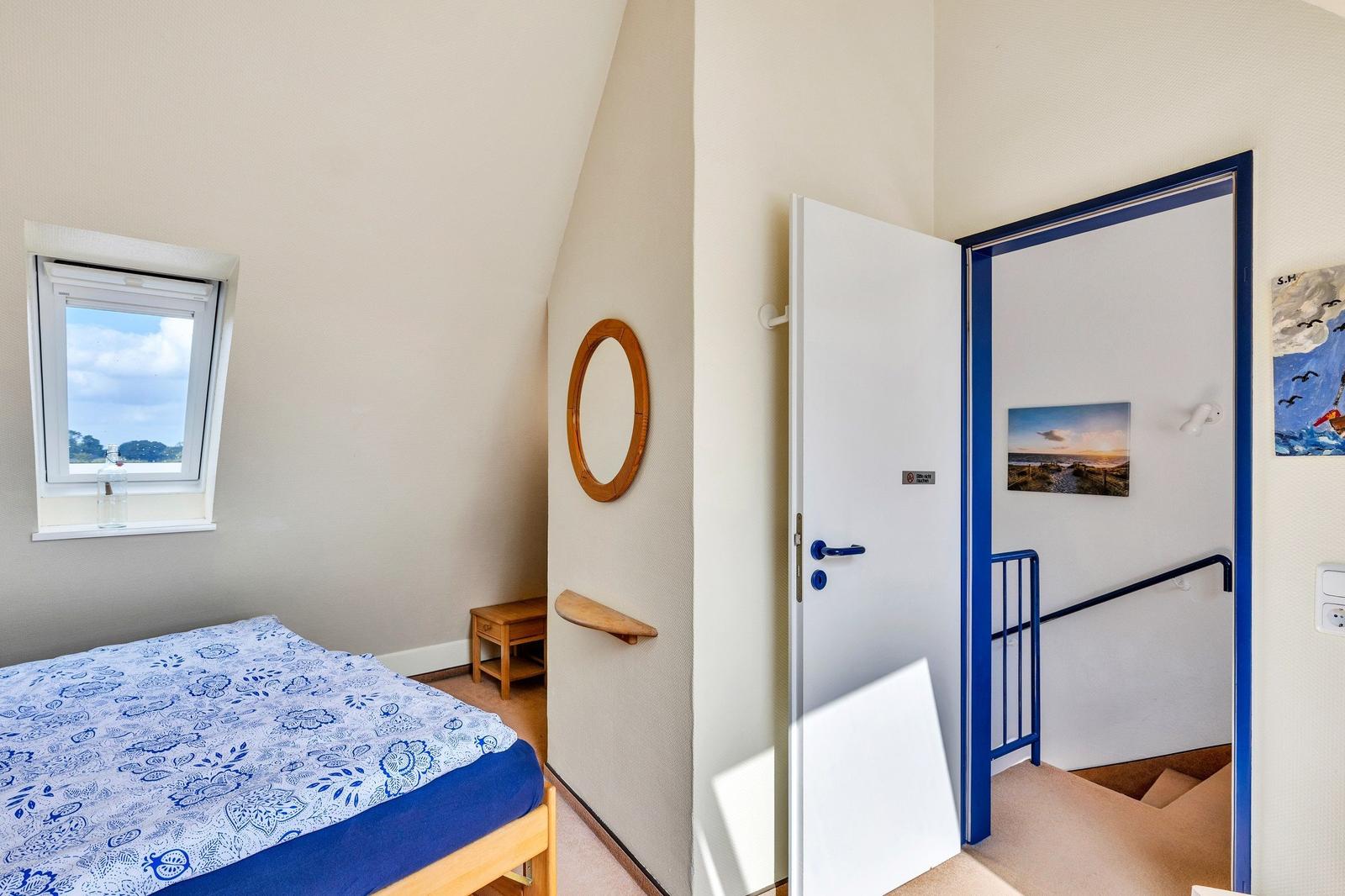 Schlafzimmer mit Bett, Fenster und Tür zu Treppenhaus.