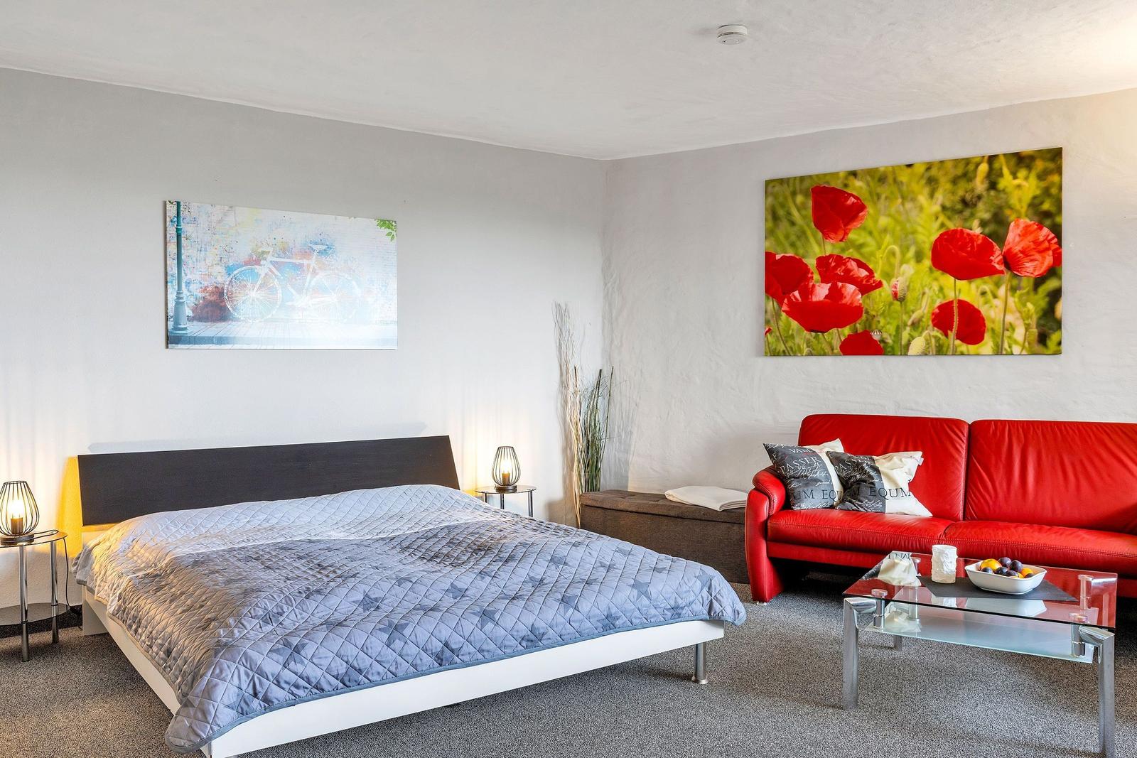 Schlafzimmer mit Bett, rotem Sofa und Wandbildern