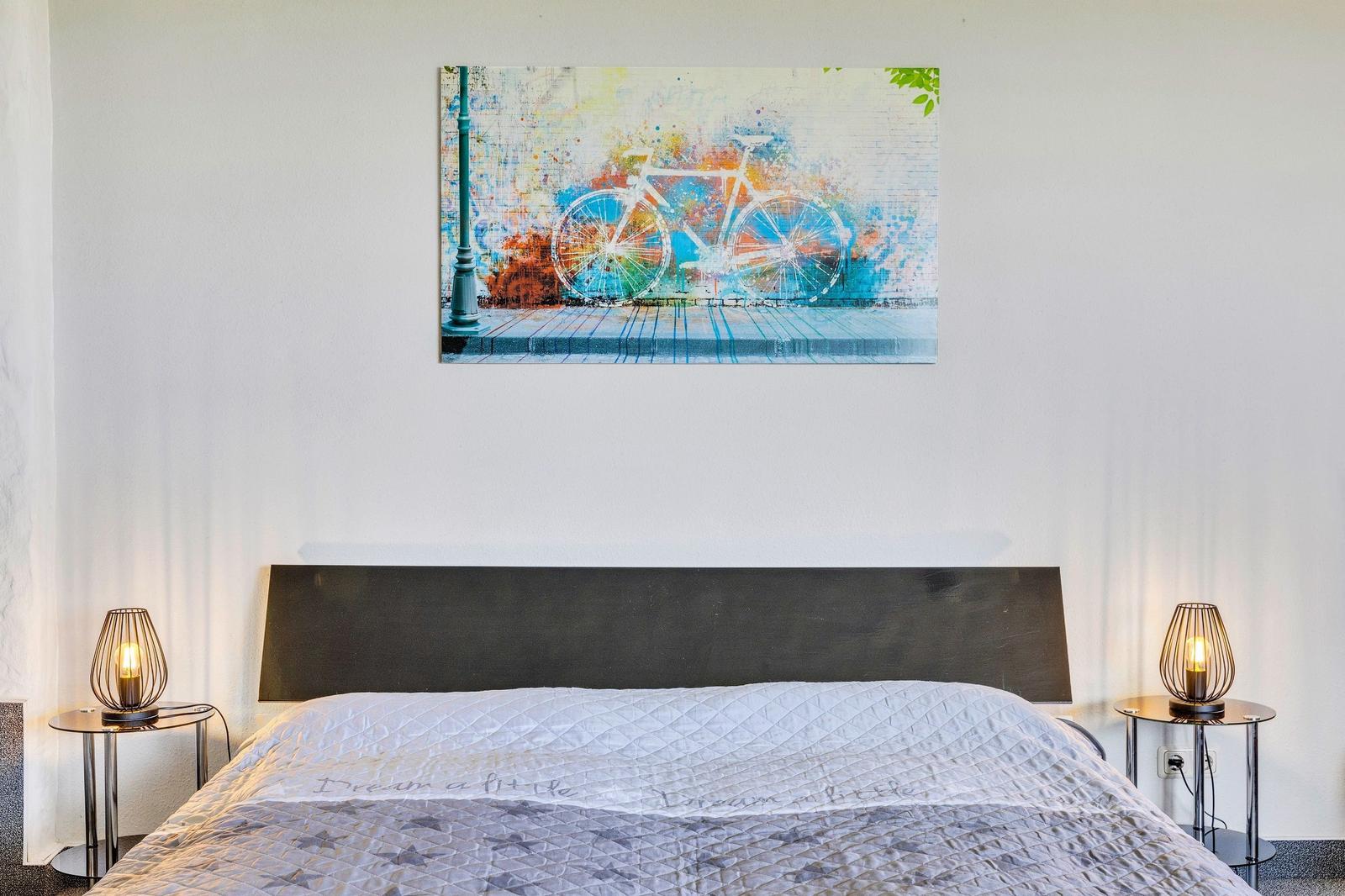 Schlafzimmer mit Bett, Nachttischen und Wandbild mit Fahrrad