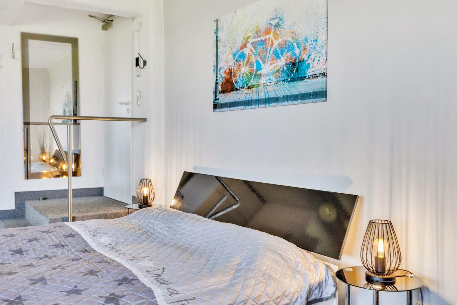 Schlafzimmer mit Bett, Nachttisch und Wandbild mit Fahrrad.