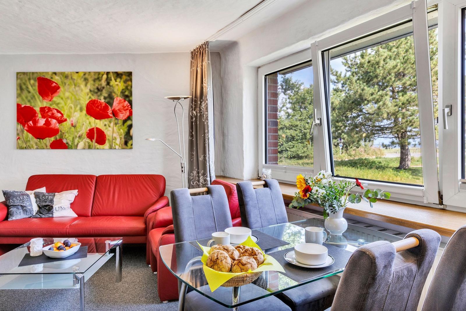 Ein Wohn- und Essbereich mit rotem Sofa, Glas-Tisch und Blick auf Grün.